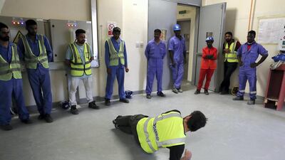 Fitness instructor Hannes Loubser demonstrates a side plank to Dewa construction workers. Photo: Pawan Singh / The National