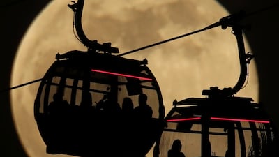 Emirates cable cars are silhouetted against the backdrop of the moon in Greenwich, London. PA via AP