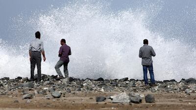 People watch the high tides near the sandy beach in Fujairah. Below, children play with rising waves caused by the tropical Cyclone Ashobaa crashing along the coast in the Omani capital, Muscat. Pawan Singh / The National; Mohammed Mahjoub / AFP