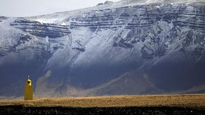 The sun shines on a yellow lighthouse on the outskirts of Reykjavik harbour.
