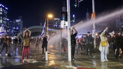 Protesters stand with their arms up as police fire a water cannon in Tel Aviv. Reuters