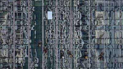 Workers clean a building’s glass wall bearing a reflection of other buildings at a financial district in Beijing. Kim Kyung-Hoon / Reuters