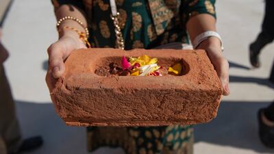 A woman carries a brick to be placed at the site of the BAPS Hindu Mandir temple after a prayer ritual.