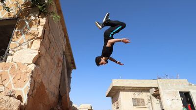 Residents watch as a young Syrian man parkours over the ruins of a building destroyed during past shelling by pro-regime forces, in the town of Binnish in the country's northwestern Idlib province. AFP