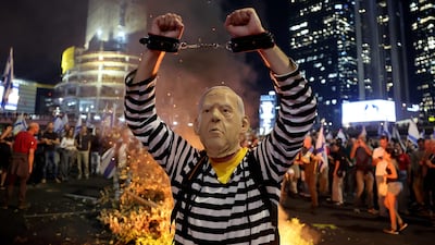 A person wearing a mask with the face of Israeli Prime Minister Benjamin Netanyahu gestures with handcuffs as protesters block a road in Tel Aviv. AFP