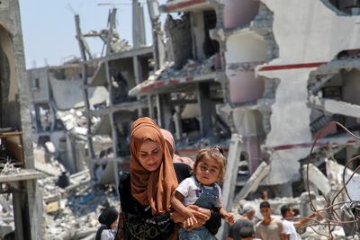 A Palestinian woman holds her daughter as she walks past the rubble of houses destroyed during the Israeli military offensive in Khan Younis in the southern Gaza Strip. Reuters
