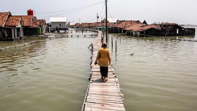 A woman walks across a bridge past houses partially submerged in seawater due to tidal flooding at the Timbulsloko village in Demak, Central Java. AFP
