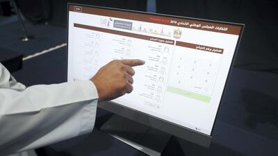 An official shows voters how to find their candidate on a blank test system. Each name and candidate number is displayed and many have been campaigning with their numbers printed prominently on billboards and posters across their emirate