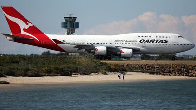 Two people watch from a beach as a Qantas plane taxies on the runway at Sydney Airport. AP Photo