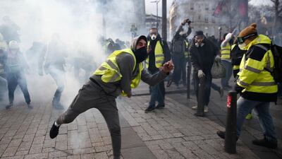 A protestor wearing a yellow vest (gilet jaune) throws a tear gas canister back at police during a protest in Paris last week. AFP