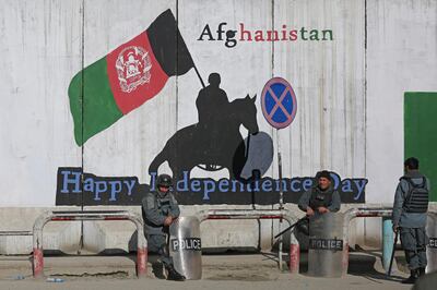 Afghan policemen in riot gear sit in front of a mural. AP