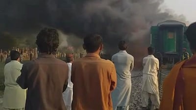 Men look at a burning train after a gas canister passengers were using to cook breakfast exploded, near the town of Rahim Yar Khan in the south of Punjab province, Pakistan, in this still image take from video obtained from social media. REUTERS
