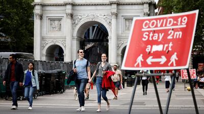 Pedestrians walk past a sign asking people to social distance, near Marble Arch in central London. AFP