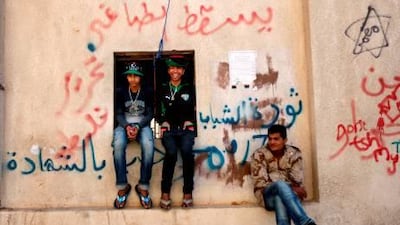 Benghazi's intellectuals have been studying and discussing for weeks to devise a plan for the future of a post-Qaddafi Libya. Above, rebels sit on a wall covered in graffiti mocking Qaddafi in Benghazi yesterday.