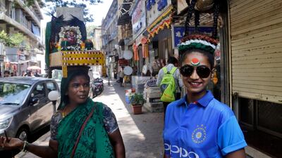 An Indian who goes around carrying an idol of Hindu goddess Lakshmi on her head looks at a cricket fan who got her hair styled for the cricket world Cup in Mumbai, India. AP Photo