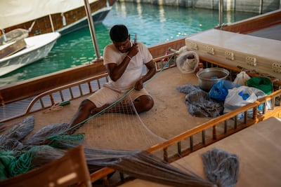 A man on a wooden boat at harbour in Doha bay sews a fishing net to be sold in Souq Waqif market. AP Photo