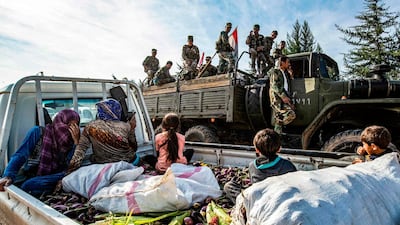 Syrian government soldiers ride in the back of a truck with national flags past a pickup truck carrying women and children seated above harvested aubergines and maize, as government forces deploy for the first time in the eastern countryside of the city of Qamishli in the northeastern Hasakah province. AFP