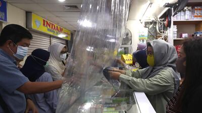 Shop attendants serve customers behind a sheet of plastic installed to help curb the spread of the coronavirus at a pharmacy in Jakarta, Indonesia. AP Photo