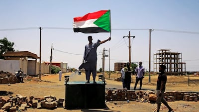 A Sudanese protester holds a national flag as he stands on a barricade along a street, demanding that the country's Transitional Military Council hand over power to civilians, in Khartoum, Sudan. Reuters