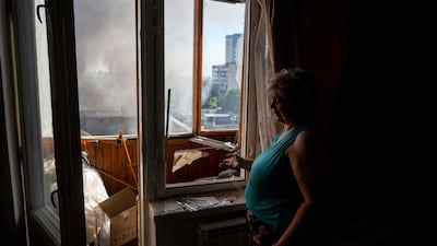 A Kyiv resident looks on a bombed landscape through a damaged window in her flat. AFP