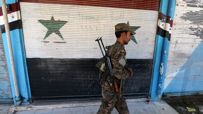 A fighter from the Syrian Kurdish YPG militia walks past a shop with Syrian national flags painted on its shutter in the city of Qamishli. Rodi Said / Reuters / April 22, 2016