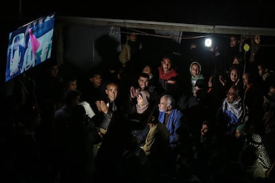 TOPSHOT - Huda Abu Jazar (C), watches her son and captain of the Palestinian national football team, Ihab Abu Jazar, during the FIFA Arab Cup 2025 group stage, Group A, football match between Syria and Palestine in Qatar, as she sits with others in a displacement camp west of Khan Yunis, in the southern Gaza Strip on December 7, 2025. Coach Ehab Abu Jazar is guiding a national team that carries on its shoulders all the hopes and sorrows of Palestinian football, but it is his mother, forced by war to live in a Gaza tent, who is his main inspiration and motivation. The war that broke out following Hamas's attack on Israel on October 7, 2023 put an end to Palestinian league matches, and left athletes in exile fearing for their loved ones in Gaza. (Photo by BASHAR TALEB / AFP)