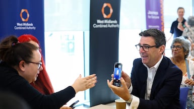 Prime Minister Andy Burnham uses a British Sign Language interpreter on a smartphone during a visit to Wolverhampton Bus Station. AFP