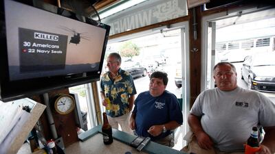 Virginia Beach residents Tom Hall, left, and Mark Janik, centre, watch as news about the Navy Seal Team Six helicopter accident is displayed on a television at a bar in Virginia Beach , Va., Saturday, Aug. 6, 2011.