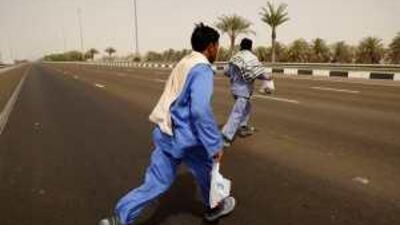 Workers cross eight lanes of traffic on highway 11, near Al Raha Mall.