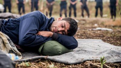A refugee, who is on hunger strike in a bid to get the Hungarian government to open its border with Serbia, rests with border guards in background. Zoltan Balogh / MTI via AP