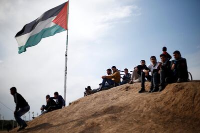 Palestinians sit near the Israeli-Gaza border fence east of Gaza City on March 29. Reuters