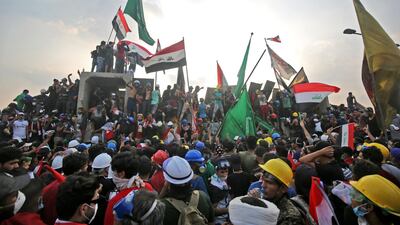 Protesters wave national flags as they stand on top of concrete barriers across Al Jumhuriya Bridge in Baghdad during anti-government protests. AFP
