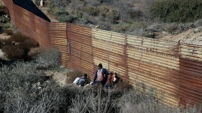 Migrant family members cross under the US border wall, aided by two local guides, in Tijuana, Mexico.. AP