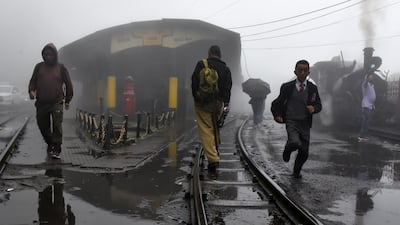 People cross the narrow-gauge tracks as a Darjeeling Himalayan Railway train prepares to depart from a station in Ghum.