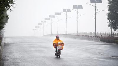 A man covered in a rain coat drives his scooter down an empty road in Jiaxing, China’s Jiangsu province. Johannes Eisele / AFP