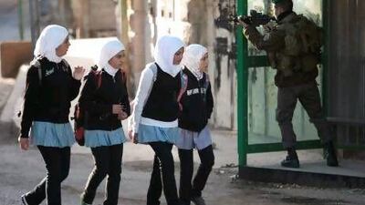 An Israeli border policeman aims his weapon as Palestinians school girls walk near a building occupied by Israeli settlers in the West Bank city of Hebron on Tuesday.