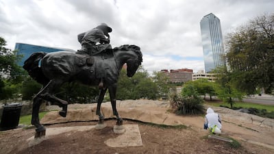 A statue on Pioneer Plaza faces towards downtown Dallas as Edwin Anzelmo, right, waits for a ride after his work shift, Tuesday, March 31, 2020. AP