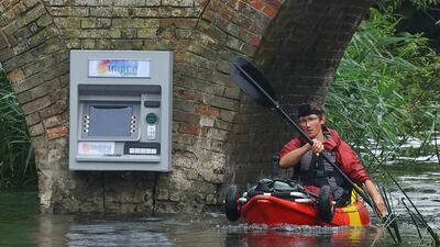 A kayaker paddles past an art installation of an ATM cashpoint by artist Impro, attached to Sonning Bridge in Sonning. Reuters