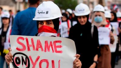 An Iraqi woman protester wearing a construction helmet adorned with the word "#Peaceful" in Arabic marches with a sign during an anti-government demonstration in the southern Iraqi city of Basra. AFP