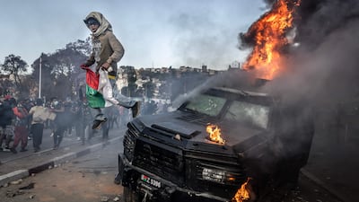 A protester holding a Malagasy flag jumps from a vandalised police vehicle in Antananarivo. AFP