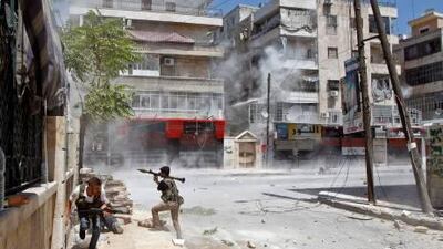 A rebel fighter prepares to fire a rocket-propelled grenade as a shell from a Syrian army tank hits a building across a street in Salaheddine.
