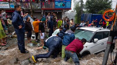 People in India help to dislodge a car stuck due to flash floods in Bhagsunag, Himachal Pradesh.