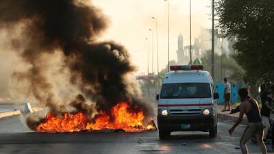 Anti-government protesters set fires and close a street while the ambulance transports injured protesters during a demonstration in Baghdad, Iraq. AP