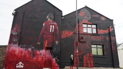 A woman poses for pictures next to a mural of Liverpool and Egypt football star Mohamed Salah outside the Anfield stadium in Liverpool, England. EPA