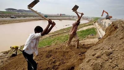 Workers building the sides of a highway in the backdrop of the Sports City Motor Race Circuit under construction in Greater Noida, India.