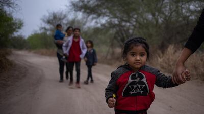 Taznari, a three-year-old asylum-seeking migrant girl from Honduras, holds her mother’s hand as they walk down a dirt road after crossing the Rio Grande river into the US from Mexico on a raft in Penitas, Texas on March 16, 2021. Reuters