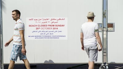 Visitors pass a sign on a wall used to fence off Jumeirah One Beach that alerts people to the closure. Antonie Robertson / The National
