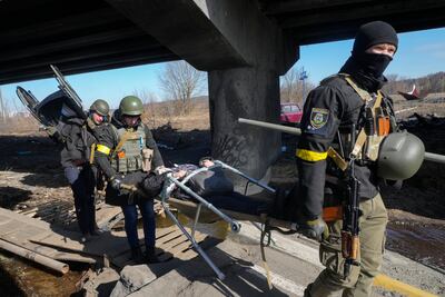 Ukrainians soldiers pass an improvised path under a destroyed bridge as they assist an elderly resident in Irpin. AP