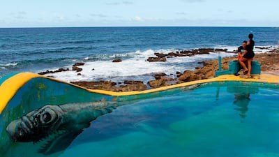 A couple stand on the ledge of a makeshift pool in the neighbourhood of La Perla where the video Suavecito was recorded in San Juan. Something unusual is happening in La Perla, a poor barrio clinging to a steep hillside between Old San Juan and the sea where the video for the pop hit Despacito was filmed. Ricardo Arduengo / AFP