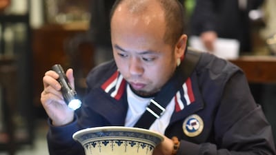 A specialist in Chinese artifacts uses a torch as he examines a large baluster-shaped vase decorated with blue deer under pines in Toulouse, during a presentation of a collection of pieces of Chinese and South East Asian art. AFP